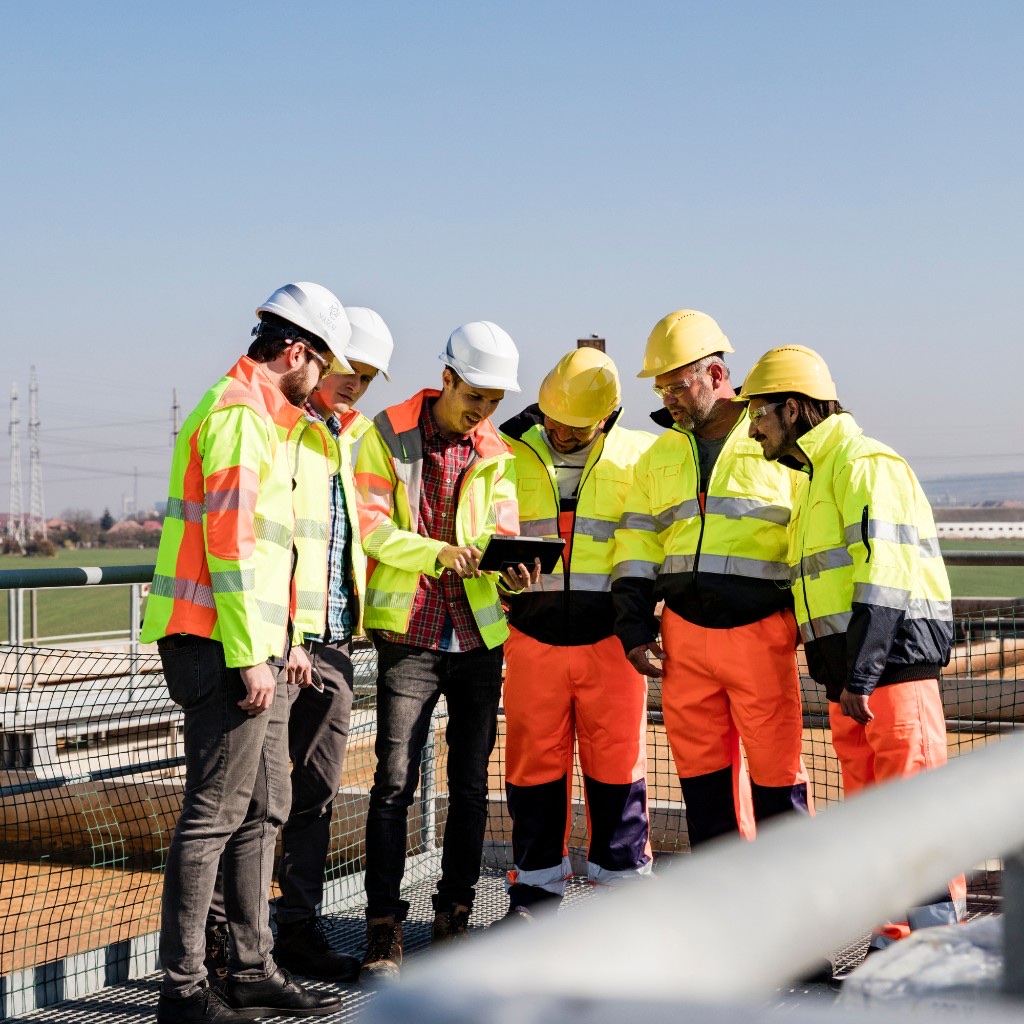 A team of engineers in safety gear reviewing a tablet at a facility