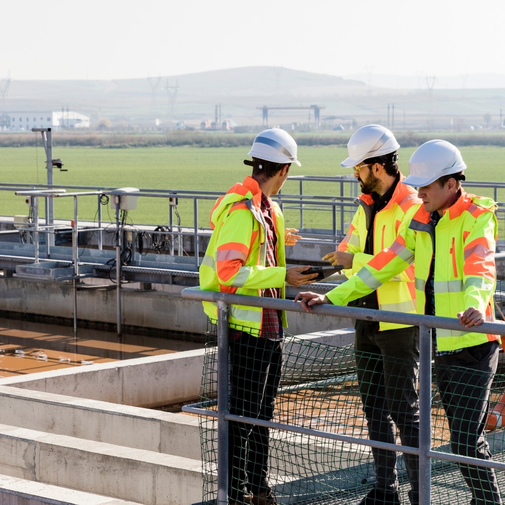 Engineers reviewing a tablet beside a wastewater treatment basin