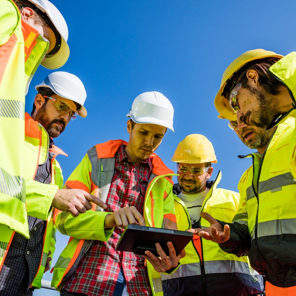 Engineers in safety gear gathered around a tablet under an open sky